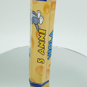 May include: A yellow and blue cardboard box with a cartoon cat on it. The box says "5 Anni" and "Viola" on it.