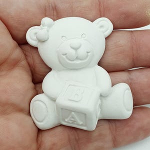 Op de afbeelding: Een witte, onbeschilderde teddybeerfiguur met een blok met de letters "A" en "B". De beer heeft een strik en is ontworpen voor knutselen of decoratie.