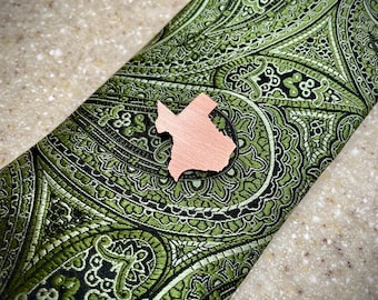 May include: A rose gold Texas state outline lapel pin on a green paisley patterned fabric.