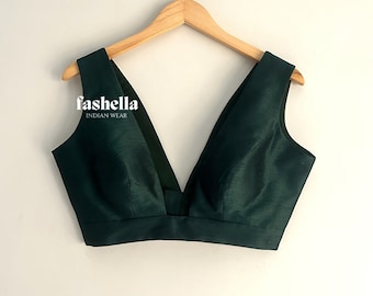 Pode incluir: Uma blusa verde escura sem mangas com um decote em V profundo, pendurada em um cabide de madeira. A blusa é feita de um tecido macio e sedoso. O texto "fasholla INDIAN WEAR" está impresso na frente da blusa.