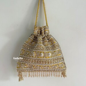 May include: A mustard yellow drawstring pouch bag featuring intricate gold embroidery, silver sequins, and white pearl bead accents. The bag has a matching yellow handle and a decorative fringe of hanging beads along the bottom edge. The text fashella is visible.