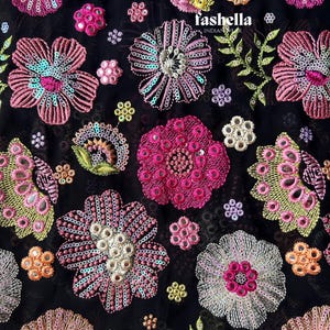 May include: Black fabric featuring embroidered floral designs in shades of pink, purple, yellow, and orange. The flowers are adorned with sequins and small mirrors. The text "fashella INDIAN WEAR" is visible.