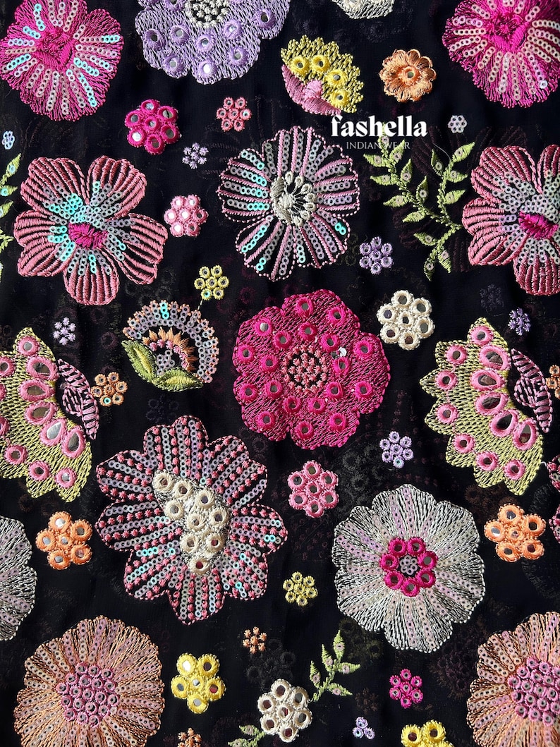 May include: Black fabric featuring embroidered floral designs in shades of pink, purple, yellow, and orange. The flowers are adorned with sequins and small mirrors. The text "fashella INDIAN WEAR" is visible.
