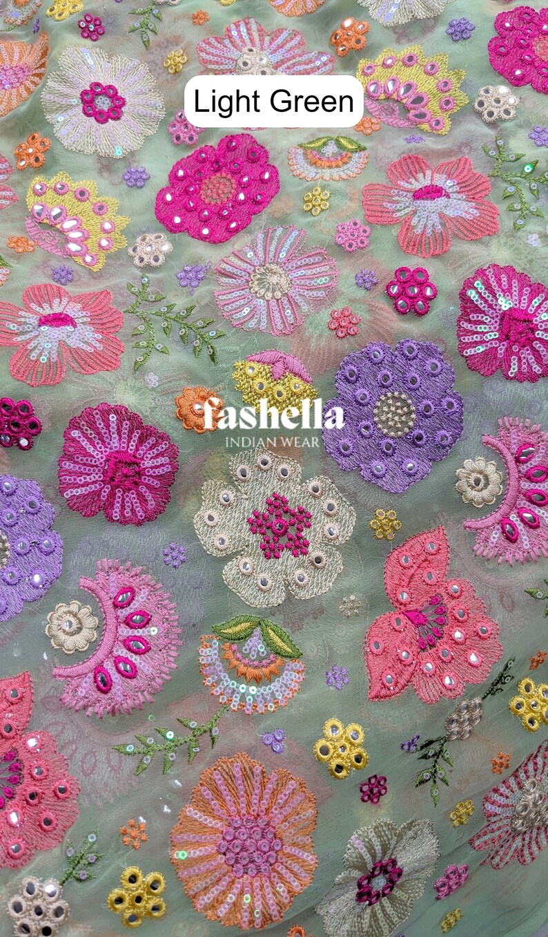 May include: Light green fabric featuring embroidered floral patterns in shades of pink, purple, yellow, and orange. The flowers are adorned with sequins and small mirrors. The fabric has the text "fashella INDIAN WEAR".