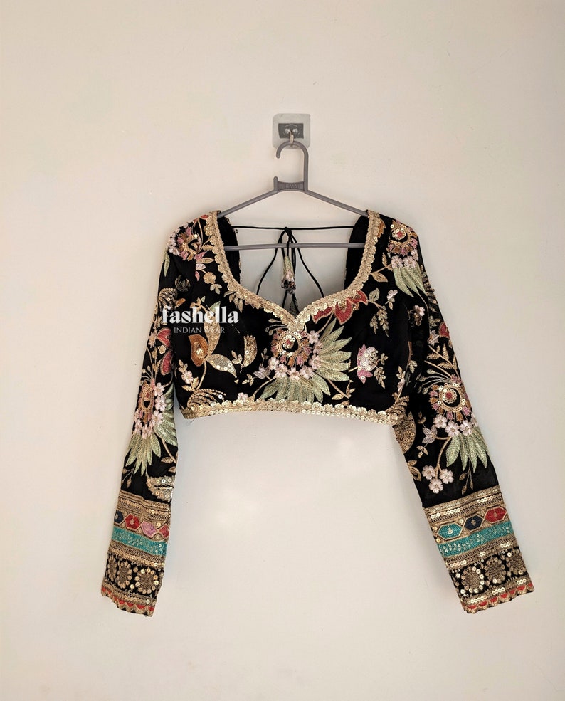 May include: A black crop top with long sleeves and a floral print. The top has gold embroidery and sequins. The sleeves have colorful trim.
