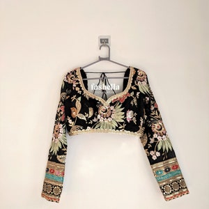 May include: Black crop top with long sleeves and floral embroidery. The sleeves have colorful trim and the top has a V-neckline. The top is on a hanger and has the text "fasholla INDIAN WEAR" on the front.