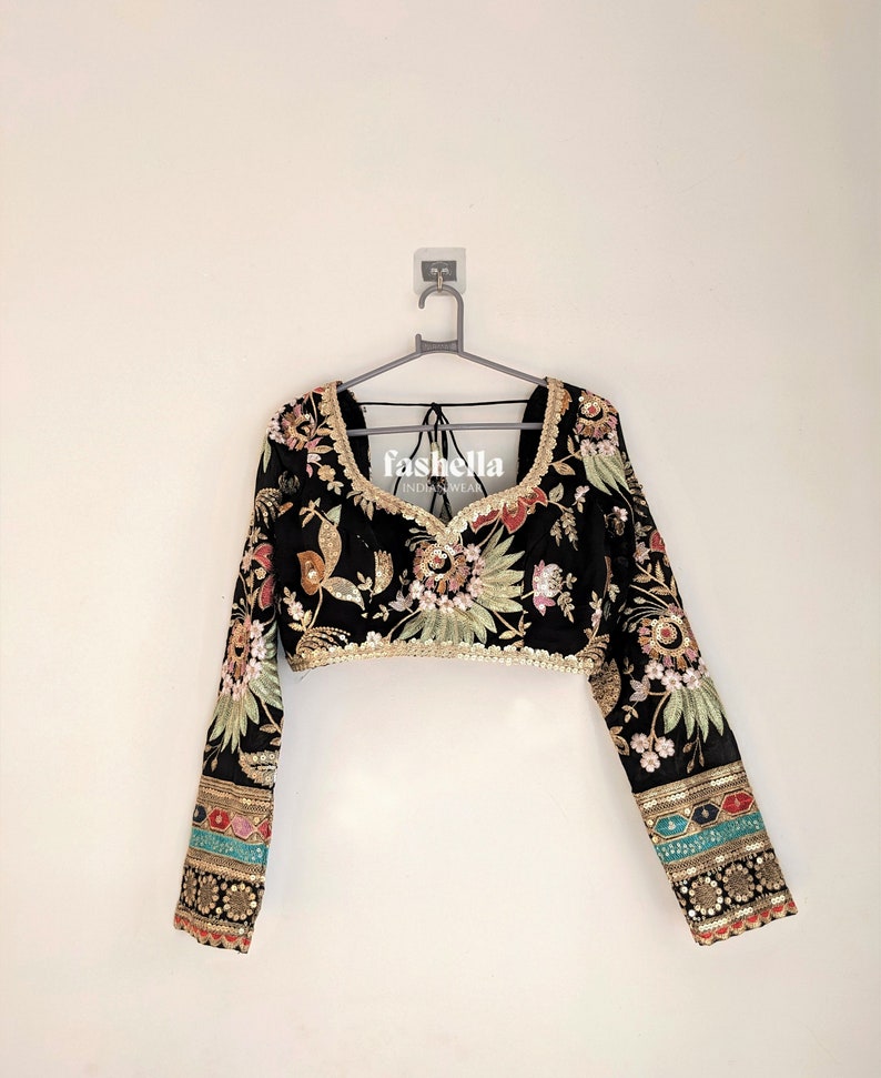 May include: Black crop top with long sleeves and floral embroidery. The sleeves have colorful trim and the top has a V-neckline. The top is on a hanger and has the text "fasholla INDIAN WEAR" on the front.