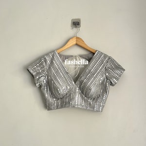 May include: A silver sequined blouse with a V-neckline and short sleeves. The blouse has a fitted bodice and is decorated with small, round sequins.
