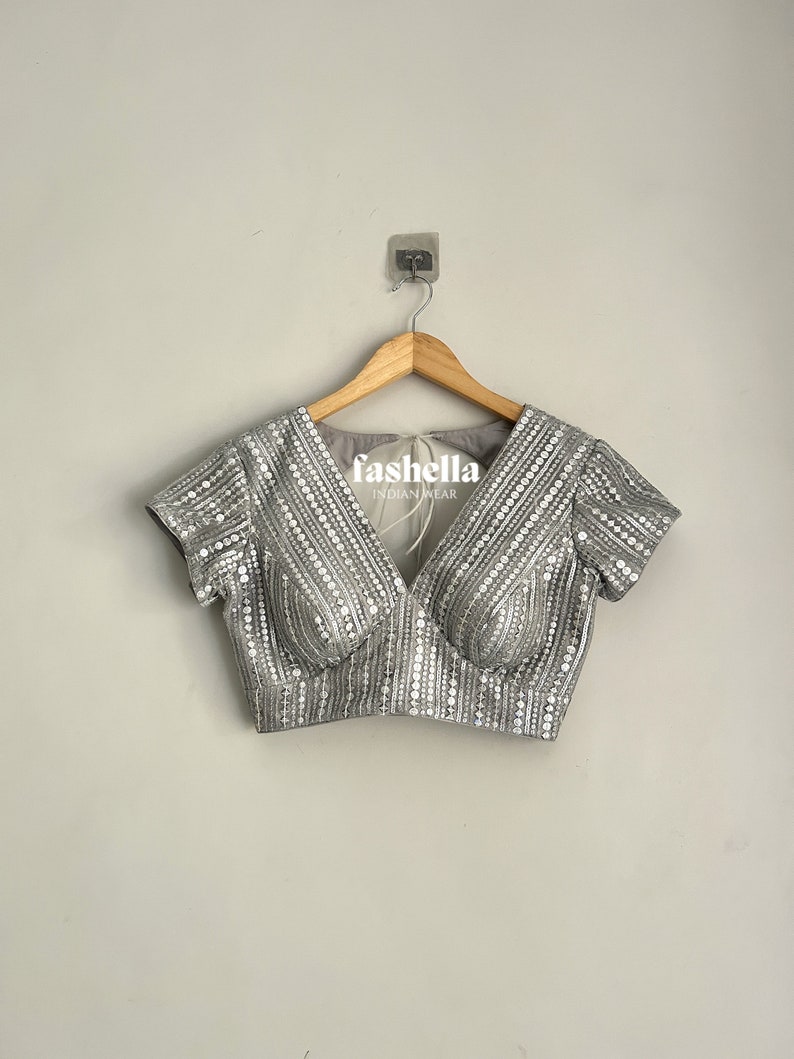May include: A silver sequined blouse with a V-neckline and short sleeves. The blouse has a fitted bodice and is decorated with small, round sequins.