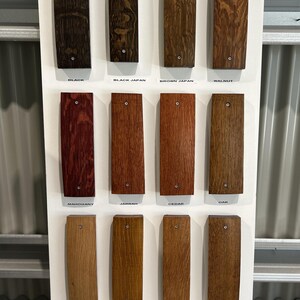 May include: A wood stain color chart with 12 different wood stain colors. The colors are labeled with their names: Black, Black Japan, Brown Japan, Walnut, Mahogany, Jarrah, Cedar, Oak, Natural Oak, Golden Teak, Old Baltic, Elm, Maple, and Teak Brown.