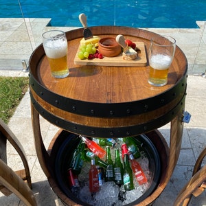 K&ouml;nnte beinhalten: Ein Holzfass-Tisch mit integriertem K&uuml;hlfach. Der Tisch hat eine obere Ablage mit einem Aufschnittbrett, zwei Gl&auml;sern Bier und einer kleinen Sch&uuml;ssel Dip. Das K&uuml;hlfach ist mit Eis und verschiedenen Flaschen Bier und Limonade gef&uuml;llt.