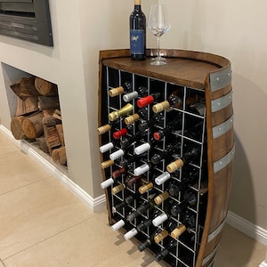 May include: A wooden wine rack made from a barrel with a metal grid to hold wine bottles. The rack is filled with wine bottles and a glass of wine is on top of the rack.