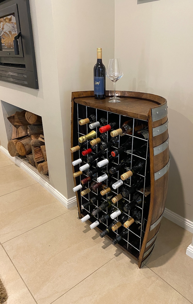May include: A wooden wine rack made from a barrel with a metal grid to hold wine bottles. The rack is filled with wine bottles and a glass of wine is on top of the rack.