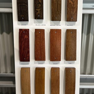 K&ouml;nnte beinhalten: Eine Holzbeizfarbkarte mit 12 verschiedenen Holzbeizfarben. Die Farben sind mit ihren Namen beschriftet: Schwarz, Schwarz Japan, Braun Japan, Nussbaum, Mahagoni, Jarrah, Zeder, Eiche, Natur Eiche, Goldener Teak, Altbaltisch, Ulme, Ahorn und Teakbraun.