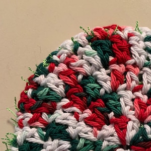 May include: A round crocheted pot holder in red, white and green with a sparkly green trim.