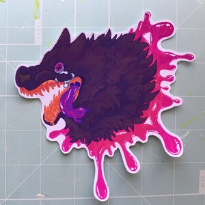 May include: A black and purple wolf with a pink tongue and fangs, with a pink splatter design behind it.