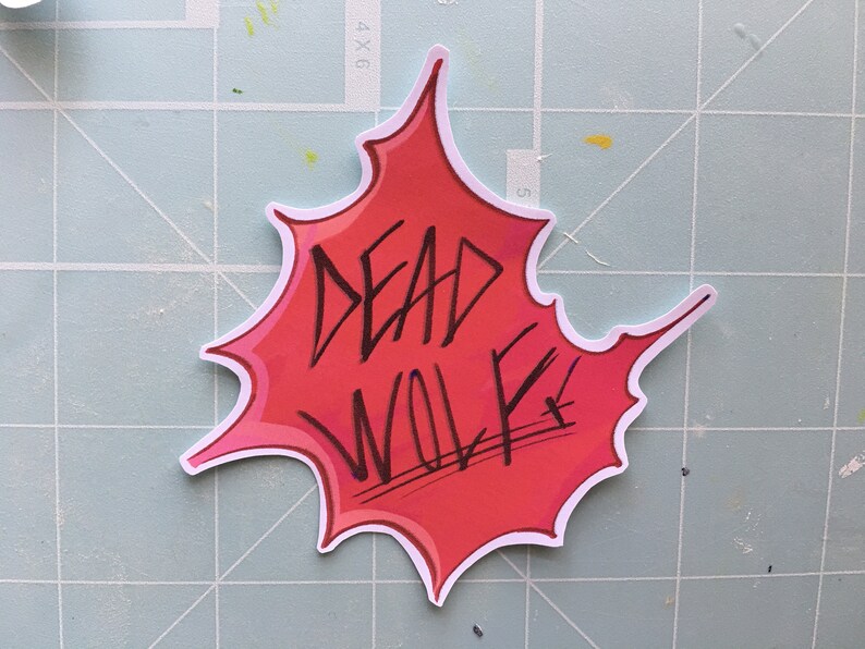 May include: A red and white sticker with a white outline in the shape of a bursting star. The sticker says "DEAD WOLF" in black marker.