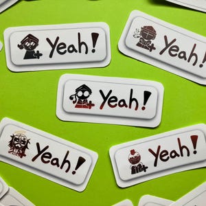 Pode incluir: Um conjunto de oito adesivos brancos com ilustrações pretas e a palavra "Yeah!" impressa em preto. Cada adesivo apresenta um personagem de desenho animado diferente.