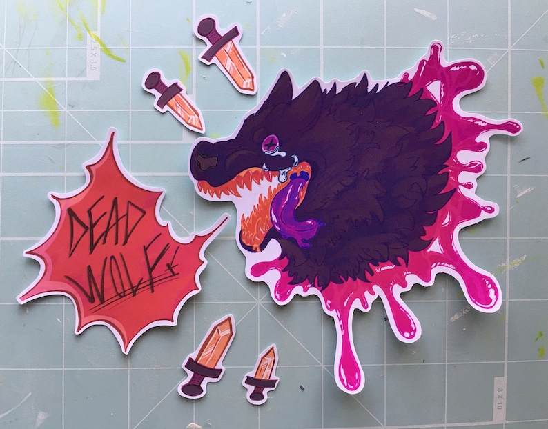 May include: A set of five stickers featuring a black wolf with a pink splatter design, three orange and brown daggers, and a red and white sticker with the text "DEAD WOLF".