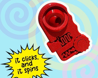 May include: A bright red, mechanical-looking device with a circular opening and a spring-like design. The text "it clicks, and it spins" is in a yellow burst graphic. The background has a swirl pattern.