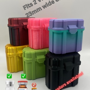 May include: Six small, stackable, plastic storage cases in various colors, including red, pink, purple, green, gold, and black. Each case has a latch and is designed to hold two vials up to 23mm wide. The text "Fits 2 Vials up to 23mm wide each" is written in white letters on a black background at the top of the image. The text "More colors available!" is written in red letters on a white background at the bottom of the image.