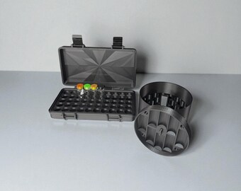 May include: A gray, open case with a geometric design, holding several small glass vials with colorful tops. Next to the case is a matching gray cylindrical container with a removable lid, also with a geometric design.