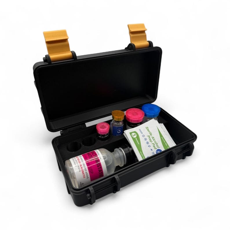 May include: Black, open, hard-shell case with yellow latches. Inside are several small bottles with colored lids, a larger bottle with a label, and alcohol prep pads. The case is designed to hold medical supplies.