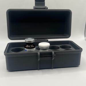 May include: A black plastic case with a latch and a foam insert for holding vials. The case contains two vials, one clear and one brown. The brown vial has a label that reads "50 ML MULTI DOSE VIAL".