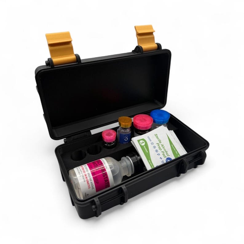 May include: A black, open, hard-shell case with yellow latches, containing vials, bottles, and alcohol prep pads. The vials have pink, blue, and yellow caps. One bottle has a pink label with white text.