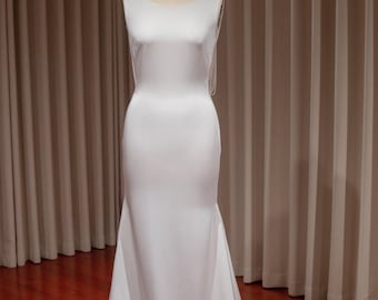 May include: A white sleeveless wedding dress with a fitted bodice and a flowing skirt. The dress is on a mannequin and has a simple, elegant design.