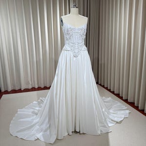 May include: A white strapless wedding dress with a fitted bodice and a full skirt. The bodice is embellished with delicate beading and floral appliques.