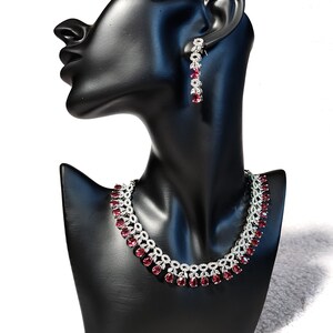 Puede incluir: Un collar y pendientes de plata con una fila de piedras rojas y transparentes. El collar est&aacute; en un busto de maniqu&iacute; negro.