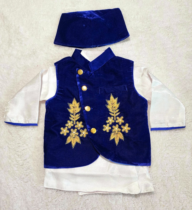 K&ouml;nnte beinhalten: Ein dreiteiliges Kinderoutfit, bestehend aus einer k&ouml;nigsblauen Samtweste mit goldener Stickerei und Kn&ouml;pfen, einer passenden M&uuml;tze und einem wei&szlig;en Langarmhemd. Die Weste hat einen Stehkragen und wird mit einer wei&szlig;en Hose kombiniert.