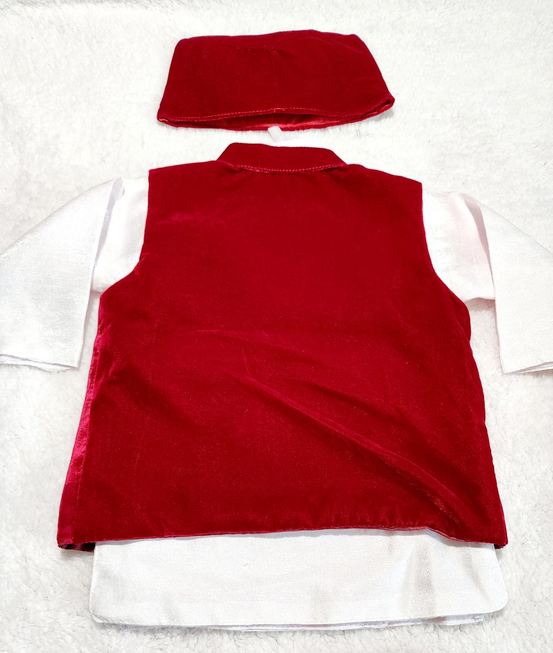 K&ouml;nnte beinhalten: Ein rotes Samt-Westen- und passendes M&uuml;tzen-Set &uuml;ber einem wei&szlig;en Langarmshirt. Die Weste hat ein klassisches Design, und die M&uuml;tze hat eine einfache, abgerundete Form. Das Outfit ist wahrscheinlich f&uuml;r ein Kind.