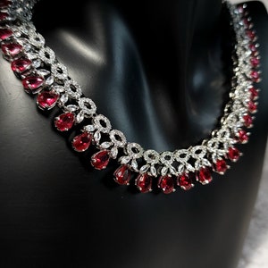 Puede incluir: Un collar de plata con una fila de piedras rojas en forma de l&aacute;grima y una fila de piedras redondas transparentes.