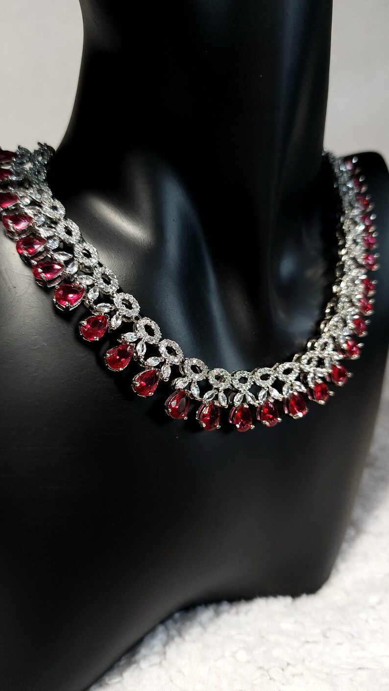 Puede incluir: Un collar de plata con una fila de piedras rojas en forma de l&aacute;grima y una fila de piedras redondas transparentes.