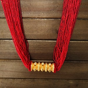 Könnte beinhalten: Eine lange rote Perlenkette mit einem goldenen Metallverschluss. Die Kette liegt auf einer Holzoberfläche.