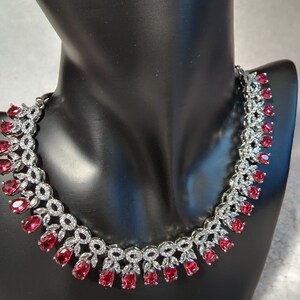 Puede incluir: Un collar de plata con un dise&ntilde;o delicado que presenta peque&ntilde;as piedras transparentes y piedras rojas m&aacute;s grandes en forma de l&aacute;grima.