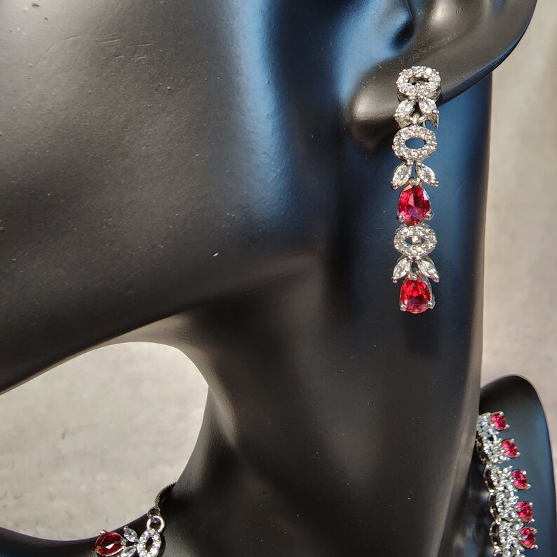 Puede incluir: Pendientes de plata con piedras preciosas rojas y piedras de circonita c&uacute;bica transparentes. Los pendientes son colgantes y tienen un dise&ntilde;o en forma de hoja.
