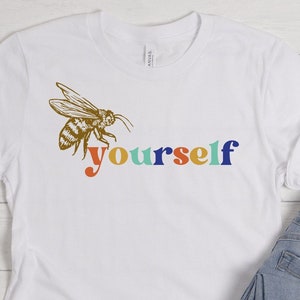 May include: White t-shirt with a bee graphic and the text "yourself" in rainbow colors.