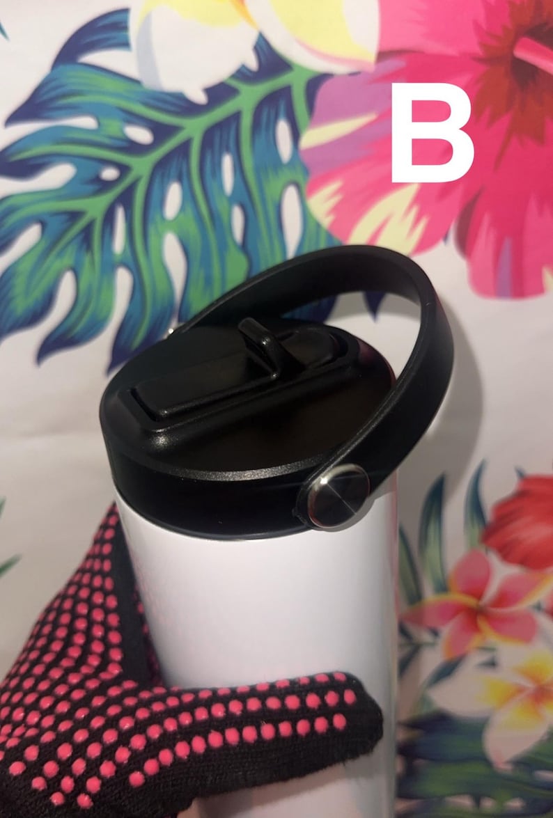 Puede incluir: Un vaso blanco con tapa y asa negras. La tapa tiene una abertura abatible. El asa est&aacute; sujeta con un bot&oacute;n plateado. La letra "B" es visible en blanco. El fondo presenta un estampado floral.