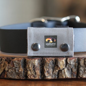 May include: A gray dog collar with a black leather strap and a gray fabric patch with a logo that says "inspired by love" and a sunset graphic. The patch has two silver snaps.