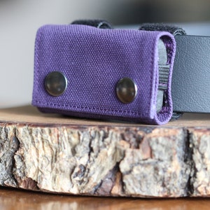 May include: A purple canvas pouch with two silver snaps, attached to a black belt.