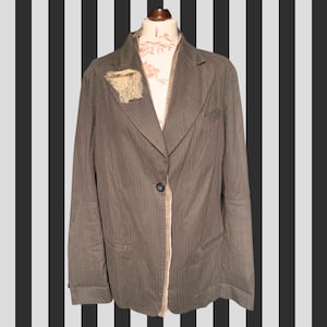 May include: A brown pinstripe blazer with a single-button closure. The blazer has a notched lapel and a decorative lace accent. The lining is a patterned fabric. The jacket is displayed on a mannequin.