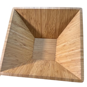 May include: A square-shaped wooden bowl made of light brown bamboo. The bowl has a slightly flared rim and a smooth, polished interior.