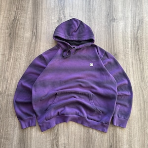 May include: Purple and black striped hoodie with a front pocket and a hood. The hoodie has a small white logo on the chest. The garment is made of a soft material.