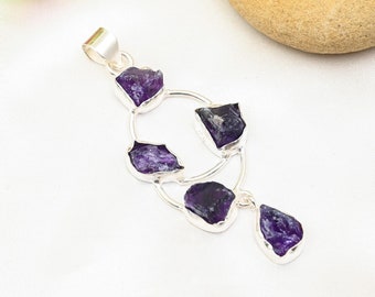 May include: A silver pendant with a circular design featuring five raw amethyst stones. The stones are a deep purple color and are set in a silver frame.