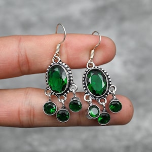 May include: A pair of silver dangle earrings with green oval-shaped gemstones. The earrings have three smaller green gemstones hanging from the larger gemstone.