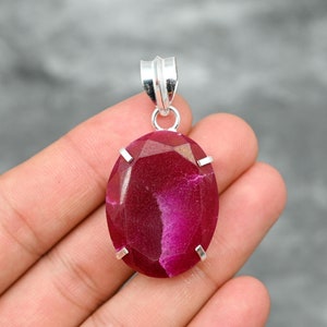 Op de afbeelding: Een zilveren hanger met een grote, ovale, gefacetteerde robijn edelsteen in een diepe roze tint. De robijn heeft een witte ader die er doorheen loopt. De hanger is gezet in een zilveren bezel met vier grijpklauwen.