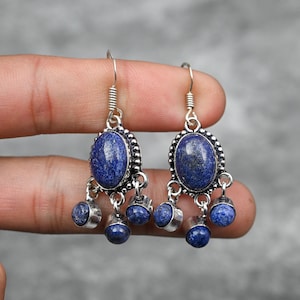 Könnte beinhalten: Ein Paar silberne Ohrhänger mit blauen Lapislazuli-Steinen. Die Ohrringe haben einen tropfenförmigen Stein oben und drei kleinere runde Steine, die darunter hängen.
